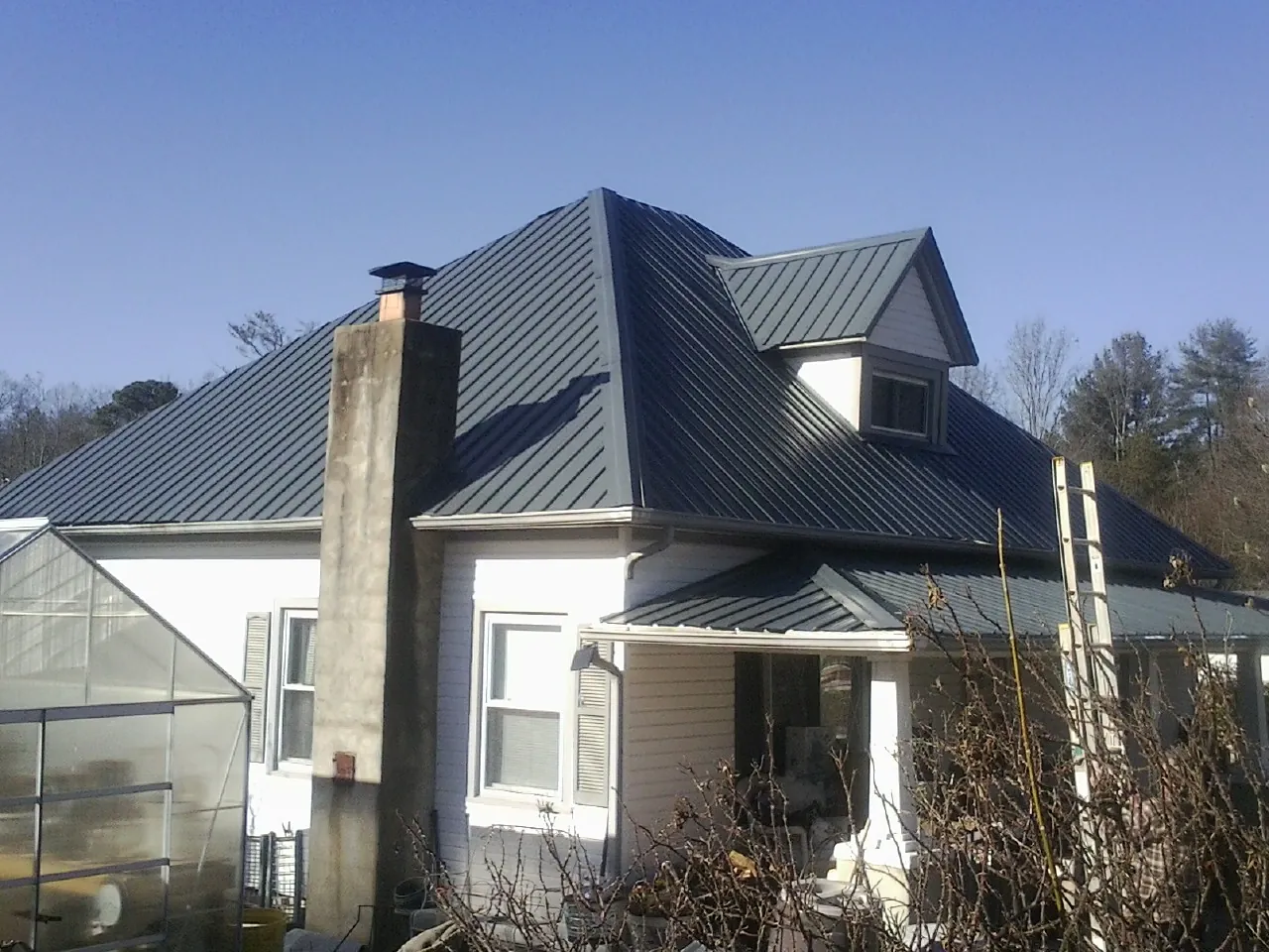 Dark blue standing seam metal roof on a white farmhouse with dormer — Slate & Tile Roof Repair by Roofing Brothers in Mamaroneck