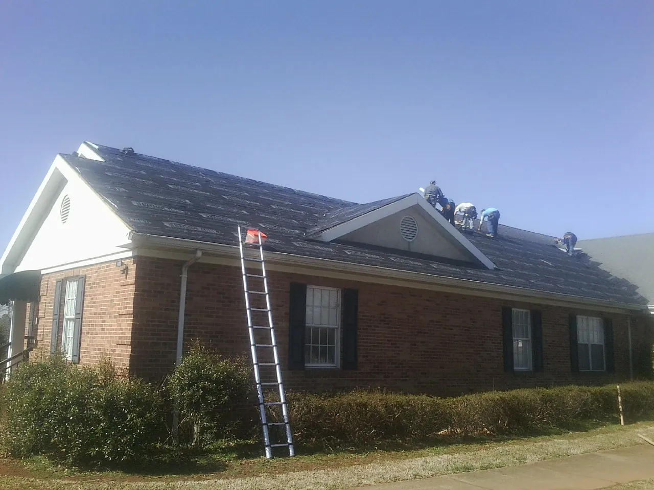 Crew tearing shingles off a brick ranch roof with a ladder set — Emergency Roof Repair work by our crew in Mamaroneck