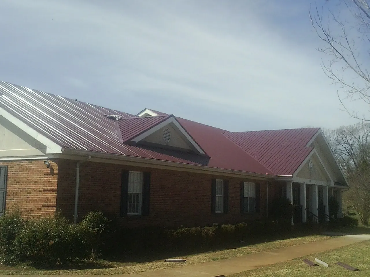 Red metal roof with gabled entries on a long brick building, from a Hail Damage Roof Repair job in Mamaroneck