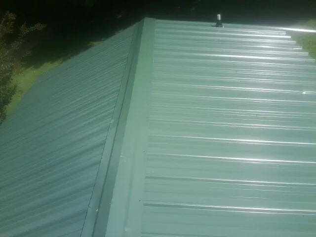 New green metal panels meeting at the ridge of a roof — Flat Roof Repair work by our crew in Mamaroneck