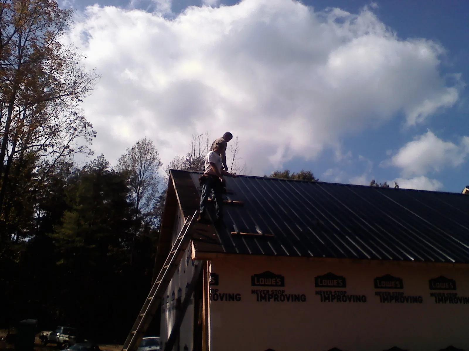 Roofer fastening dark metal panels high against a cloudy sky, from a Roof Inspection job in Mamaroneck