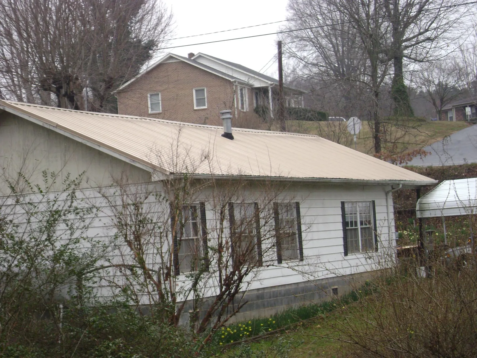Tan metal roof on a white sided house set into a hillside — Commercial Roofing by Roofing Brothers in Mamaroneck